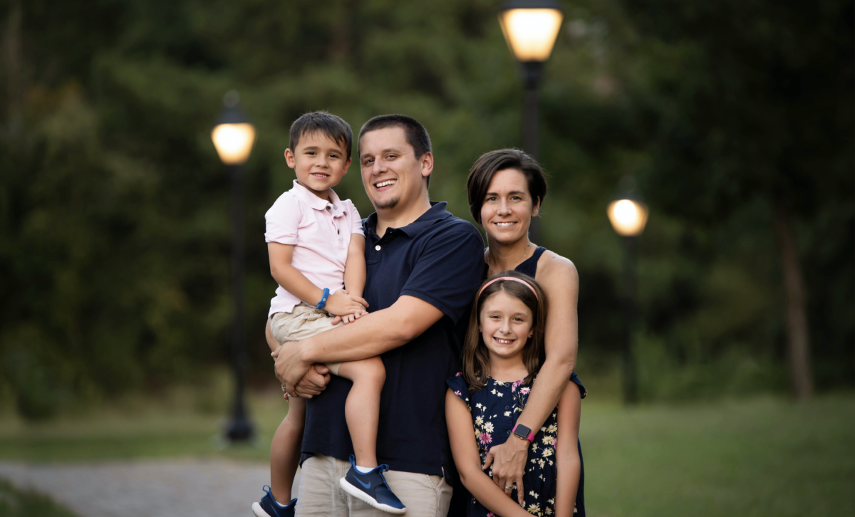 A young boy and his family stand in a park in the evening.