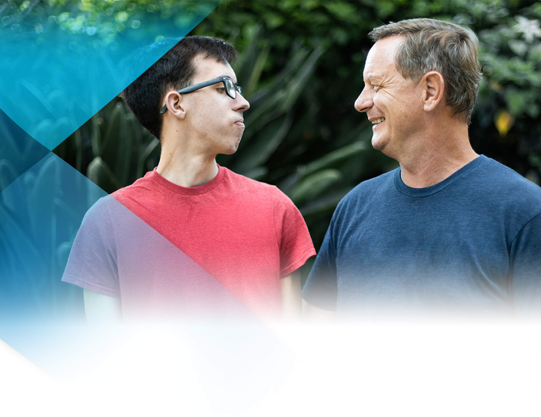 A young man in a red shirt and glasses looks at an older man in a blue shirt looking back at him.