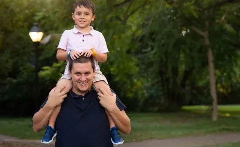 A young boy rides on his dad's shoulders.