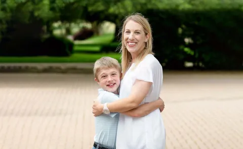 A young child embraces his mother, both smiling at the camera.